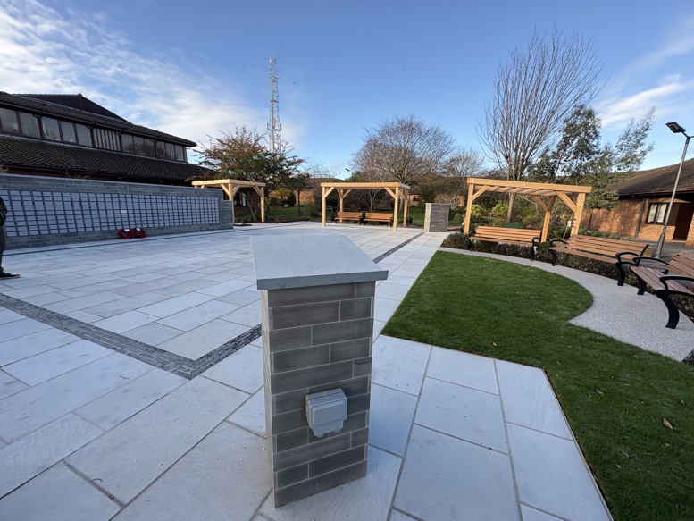 Accessible landscaped courtyard featuring paved walkways, lawn areas, timber pergolas with seating, and raised planting beds beside a modern building.