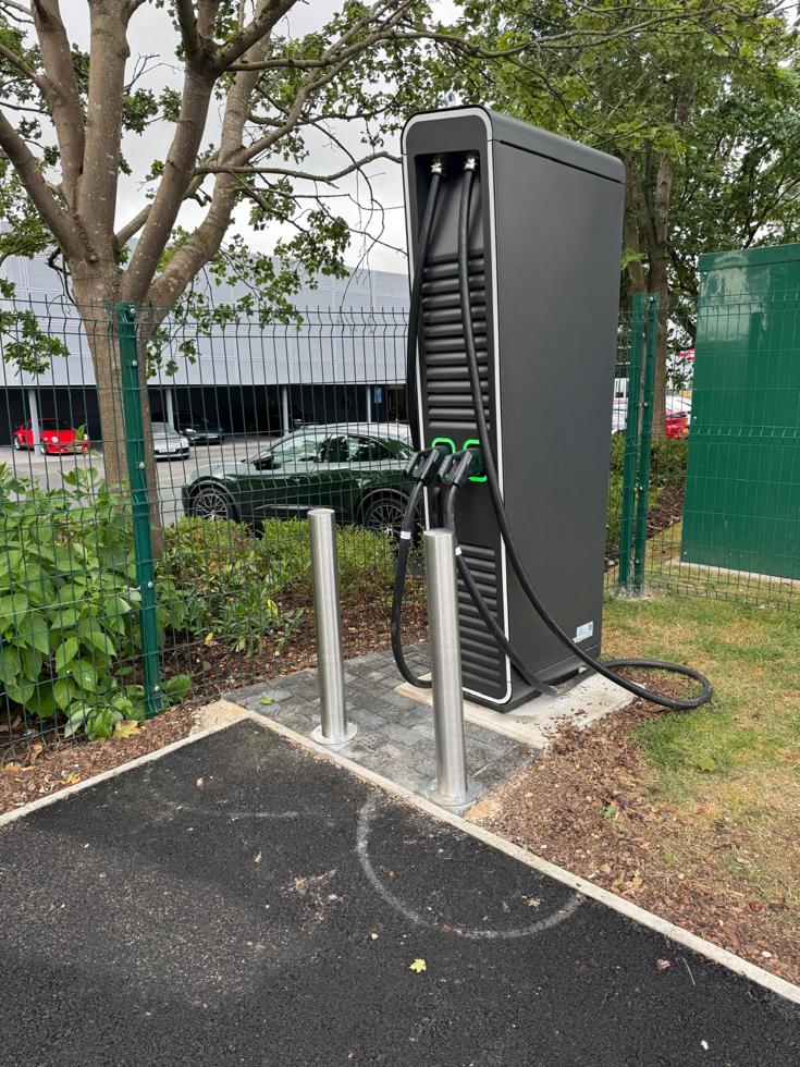 Electric vehicle charging station with charging cables in a landscaped parking area.