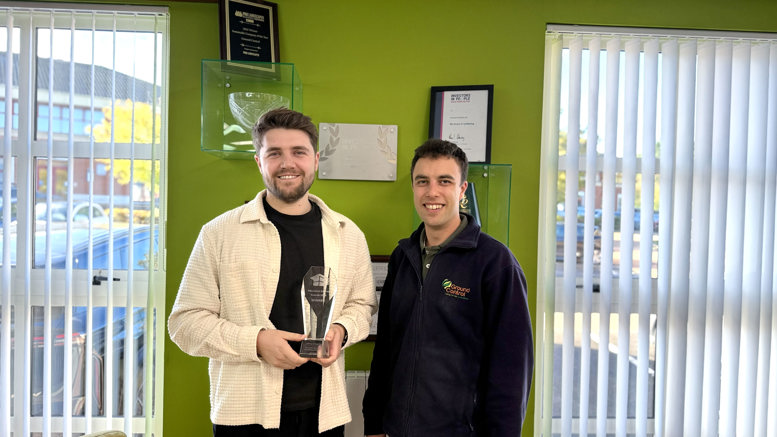Two people standing indoors, with one holding a glass award.