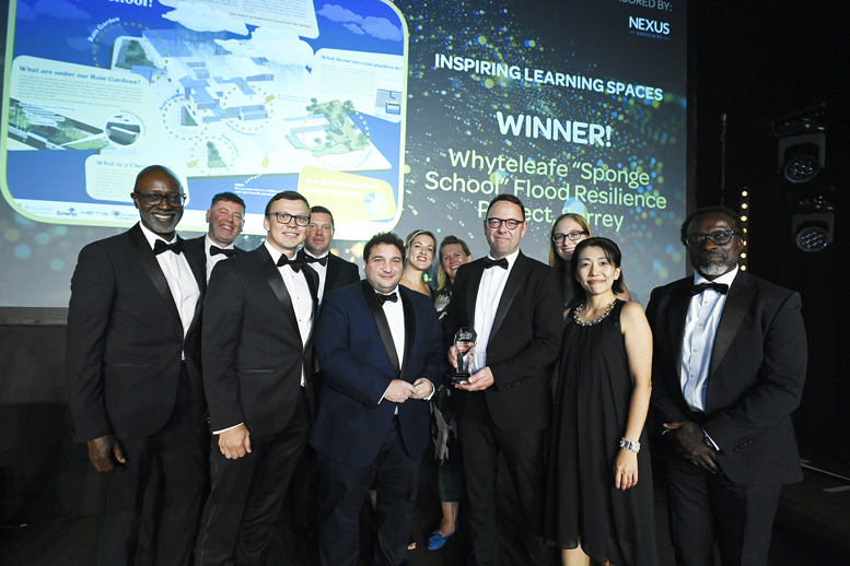 Group of award recipients on stage holding a trophy, with a screen behind announcing Whyteleafe ‘Sponge School’ Flood Resilience as the Inspiring Learning Spaces winner.